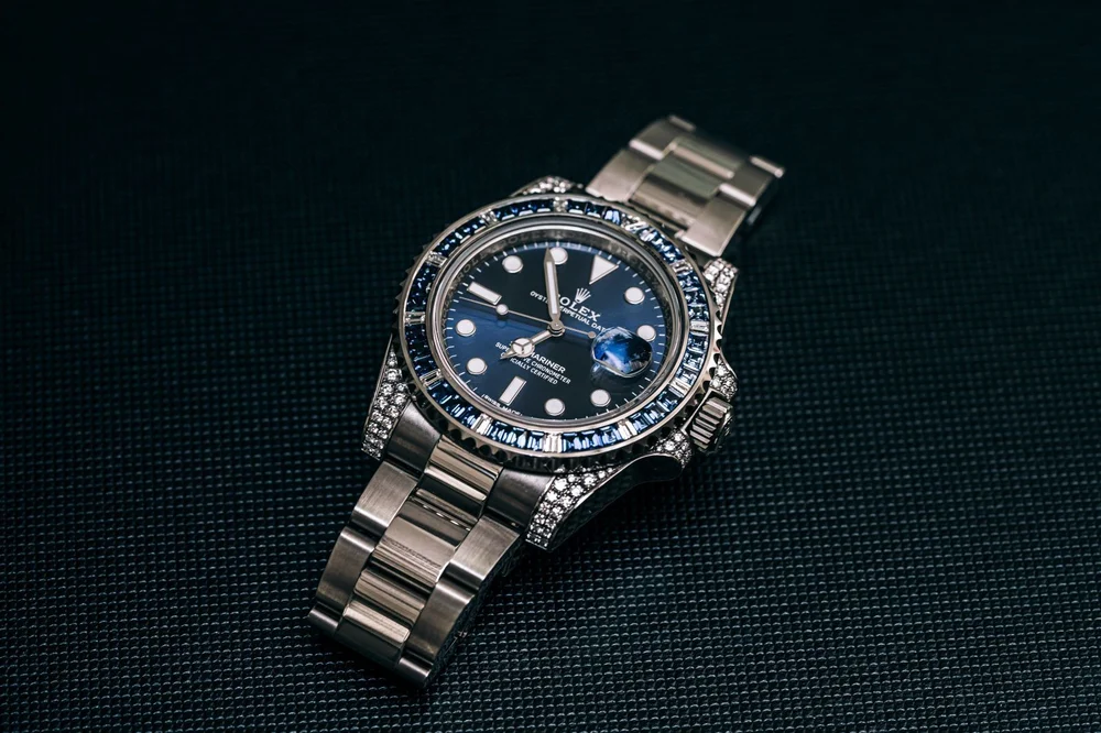 A luxury Rolex Submariner wristwatch with a blue dial, featuring a custom diamond-set case and a bezel inlaid with blue sapphires, presented on a stainless steel Oyster bracelet